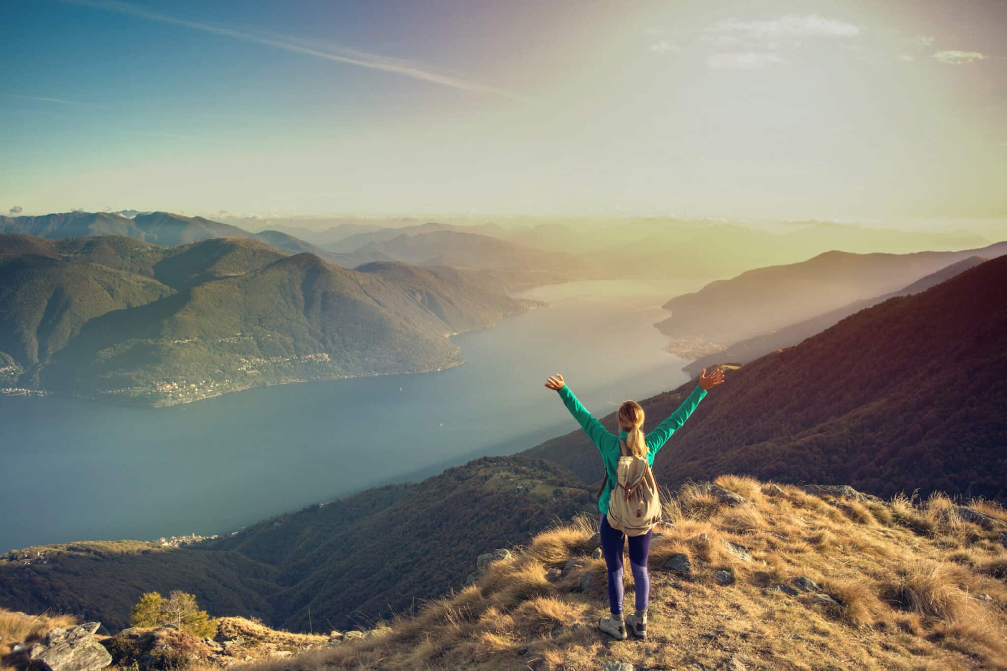 Young woman hiking reaches the mountain top, outstretches arms for success and freedom.